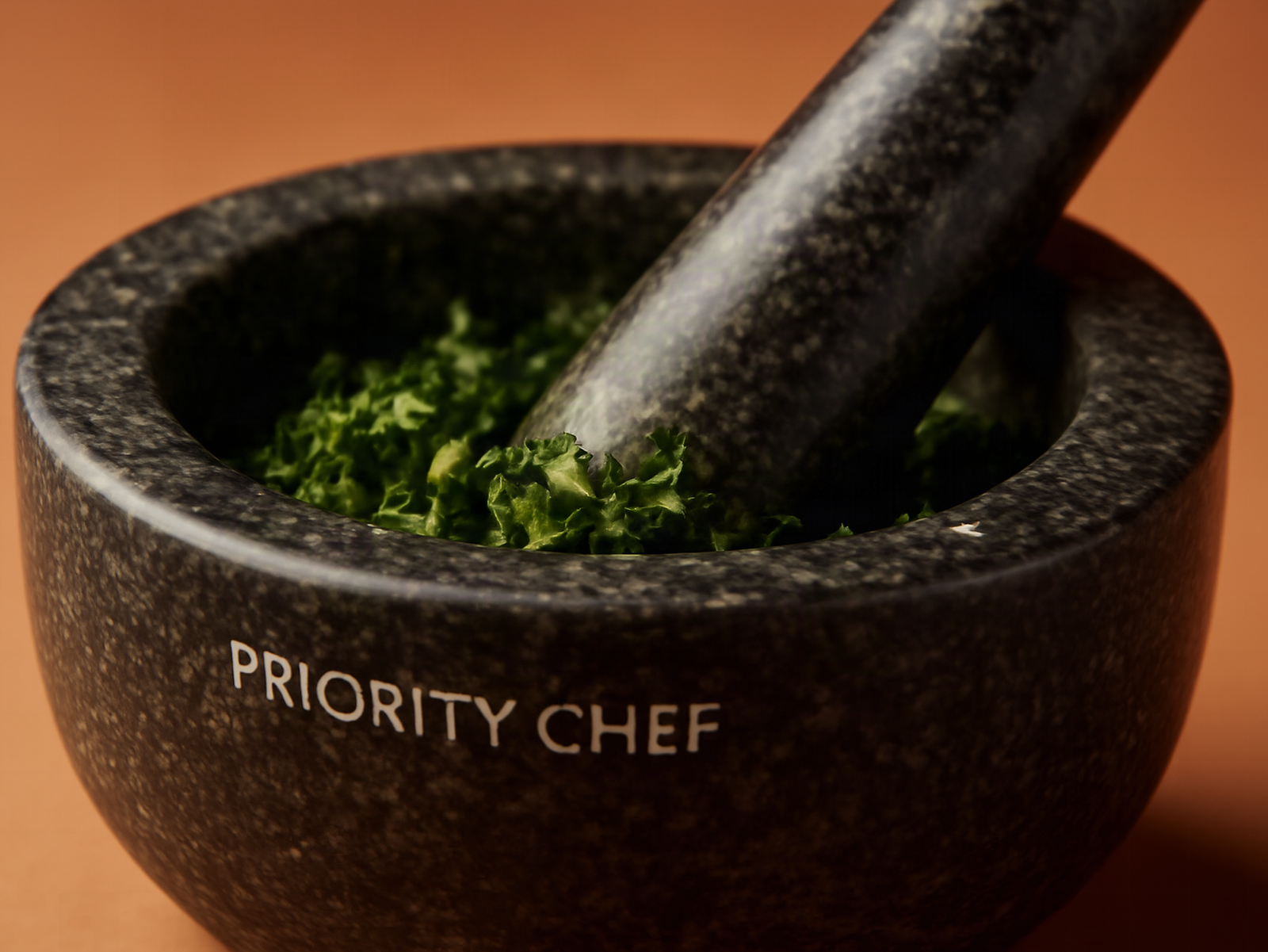 Macro close-up of black granite mortar filled with crushed herbs, pestle resting inside